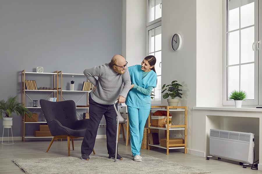 Smiling Caregiver Or Nurse Helping A Retired Senior Man Whos Wal