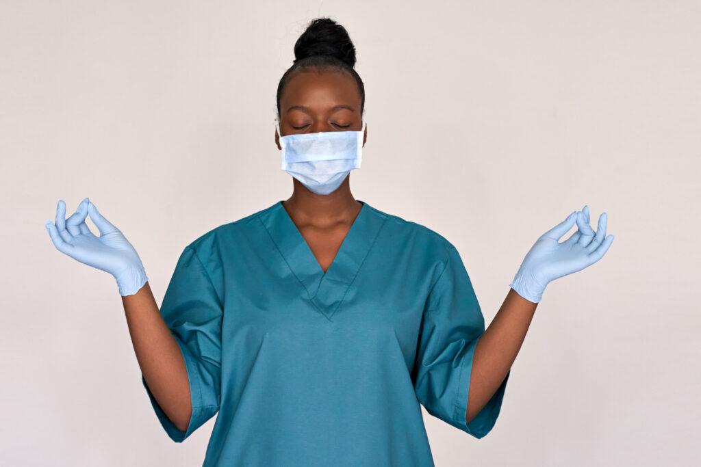 nurse in blue scrubs, a glove, and a disposable mask meditating